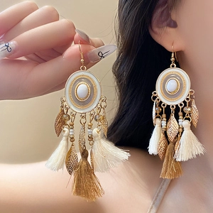 Detail of bohemian feather tassel earrings featuring white resin stone and gold leaf charms
