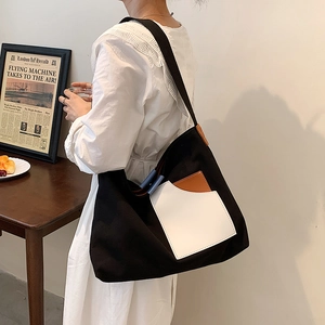 Versatile black canvas tote bag with white pocket shown in a lifestyle shoulder carry view