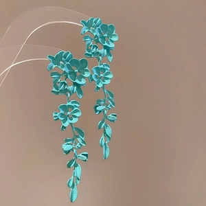 Detail view of blue-green floral earrings featuring layered metal petals and leaves