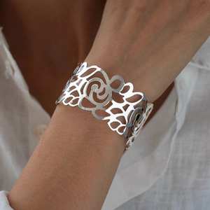 Detail shot of wide hollowed-out silver cuff bracelet with artistic floral patterns