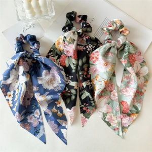 Close-up of three satin floral scrunchies with long ribbons on a stylish white background