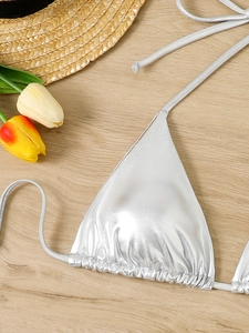 Detail of silver metallic triangle bikini top with glossy coating on light wooden background