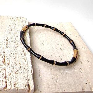 Detailed view of black and 18k gold plated bamboo style bangle on white stone
