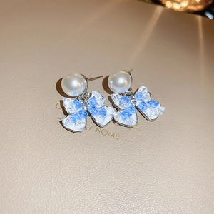 Macro detail of pearl stud earrings featuring a blue stone bow pendant on a soft background