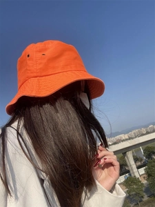 Close-up of orange cotton bucket hat with metal ventilation eyelets worn outdoors
