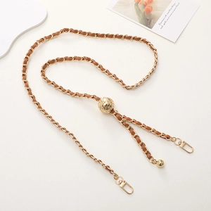 Close-up of golden metal chain with brown leather weave and spherical buckle detail