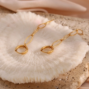 Detailed close-up of 18K gold-plated long chain earrings on a white textured coral base