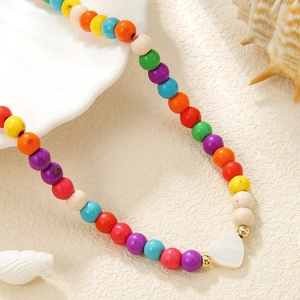 Colorful beaded necklace with white heart pendant on shell tray with coastal theme