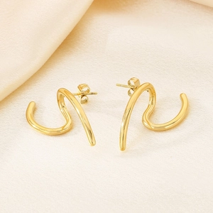 Macro shot of gold spiral S-shaped earrings on elegant cream satin fabric