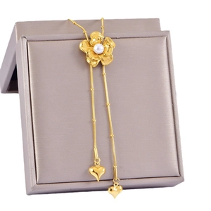 Long golden flower pearl necklace with heart tassel charms on a gray jewelry box