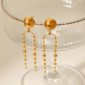 Detailed view of gold stainless steel tassel earrings hanging on elegant glass dish rim