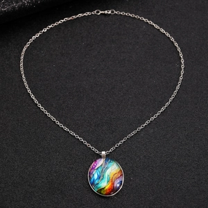Close-up of colorful round stone pendant on a silver chain over dark textured fabric