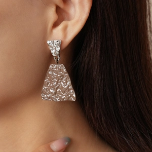 Macro detail of asymmetric geometric silver earrings with hammered texture on female model