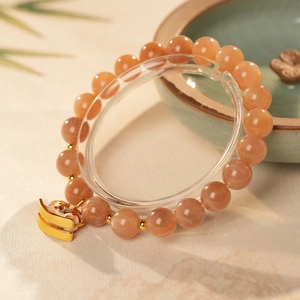 Detail of natural sunstone beaded bracelet with golden enamel charm on a display stand