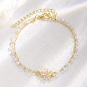 Dettaglio bracciale dorato a doppio strato con perle, cristalli e ciondolo a fiocco di neve
