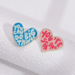 Macro shot of heart-shaped enamel brooches with motivational quotes on textured background