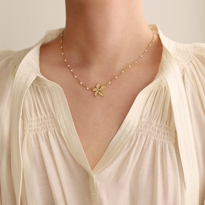 Model wearing a gold flower pendant necklace with white beads on a pleated shirt