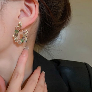 Exaggerated C-shaped gold earrings with colorful gemstones and pavé crystals on a model