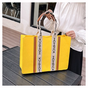 Close-up of yellow felt tote bag with MOMPICK logo webbing and brown leather accents