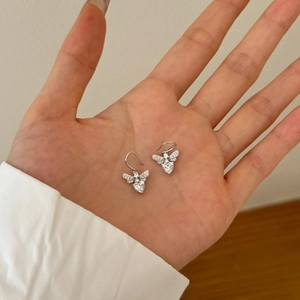 Detailed view of silver bee earrings with white heart zircon held in palm for size scale