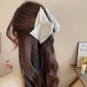 Detailed view of a white fabric hair claw with blue polka dots on long wavy brown hair