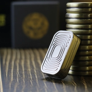 Detail of silver metallic EDC haptic coin with engraved ripples on a wooden surface