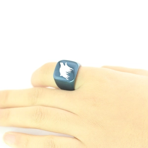 Detailed view of square blue metal ring with white forest wolf engraving on finger
