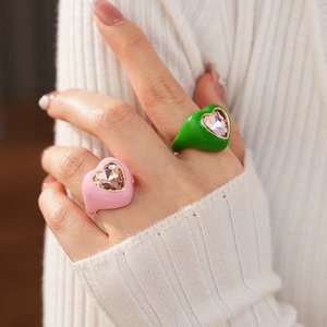 Detailed view of pink and green enamel heart rings with inlaid zircons on a hand
