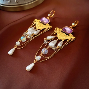 Vintage gold earrings with purple gemstone and pearl tassels on brown silk background