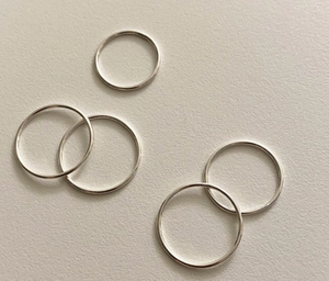 Close-up of five minimalist S925 sterling silver thin stackable rings on a textured surface