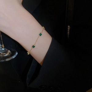Gros plan d'un bracelet doré avec pierres d'émeraude carrées porté au poignet d'un mannequin