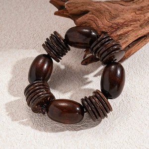 Detailed view of large oval dark wood beads and coconut shell discs on an elastic bracelet