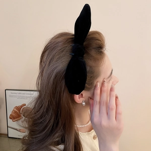 Detail view of large black velvet bow hair clip on model's long wavy hair from the side back