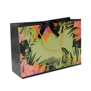 Floral paper gift bag with tropical prints, gold handles and black ribbon bow detail