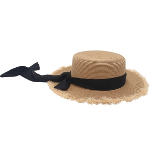 Detail of a woven straw hat featuring frayed edges and a decorative black ribbon bow