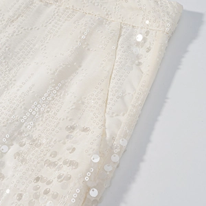Dettaglio macro del tessuto con paillettes bianco crema e strisce sulla tuta chic