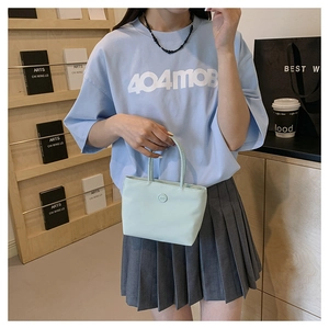 Détail du sac à main en nylon vert clair avec logo rond tenu par un mannequin en studio