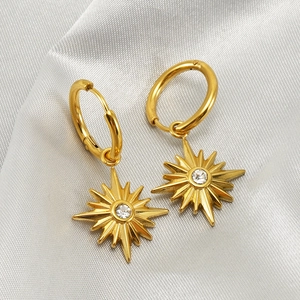 Golden hoop earrings with starburst pendants and clear zircon stones on grey silk