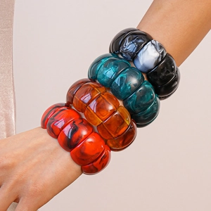 Close-up of stacked acrylic geometric bangles in marble and amber resin textures