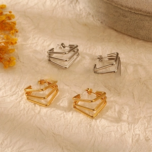 Détail de boucles d'oreilles V géométriques en or et argent sur fond beige texturé