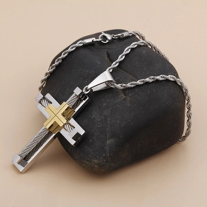 Detail of silver stainless steel cross pendant with gold inlay on black pebble stone