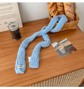 Blue knit scarf with VEGETABLE label on wooden table with coffee beans and bread