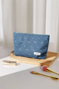 Detail of blue denim makeup bag featuring white heart and bow patterns and logo label