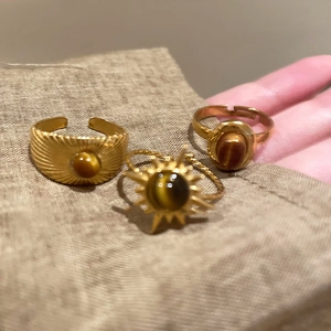 Three gold oval rings with tiger eye stones set on a rustic brown burlap background