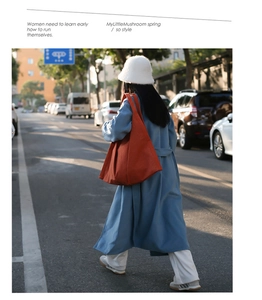Street style view of a large orange canvas tote bag paired with a long blue coat