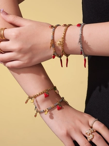 Detail of stacked gold beaded bracelets with strawberry, chili and sun enamel charms