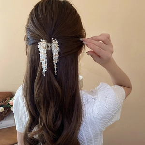 Detail showing artificial pearl tassel hair claw clip worn on a woman's hair