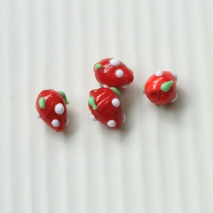 Macro shot of four red strawberry-shaped glass beads with green leaf details