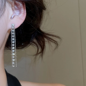 Dettaglio di orecchini a nappa in argento con strass scintillanti indossati da una modella