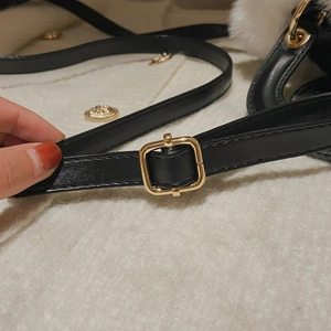 Detail of adjustable black leather strap with square gold metal buckle on faux fur